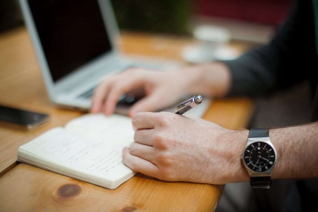 Person Writing in a book With a pen on his table